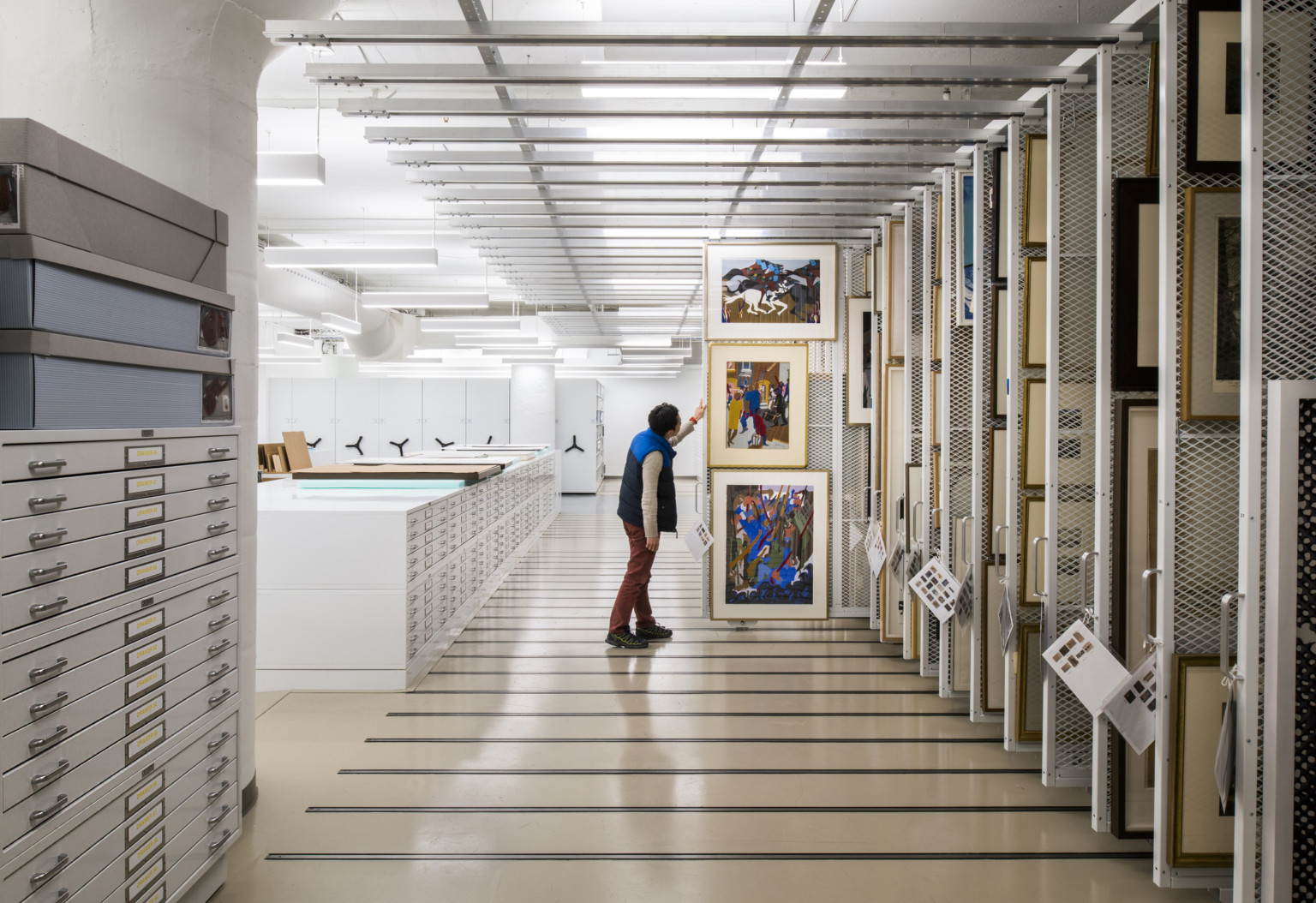 In a storage room for flat artworks to either lay in drawers or hang on movable wall, a man has pulled out a storage wall