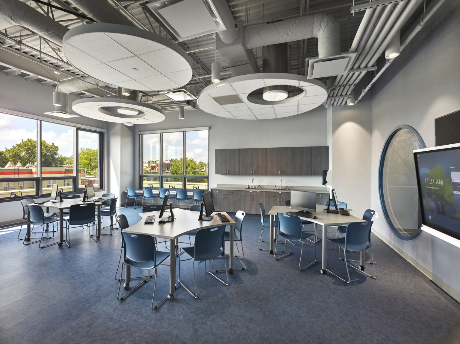 Irregularly shaped tables with chairs and computers in white corner room. Ducts and round panels above, round interior window