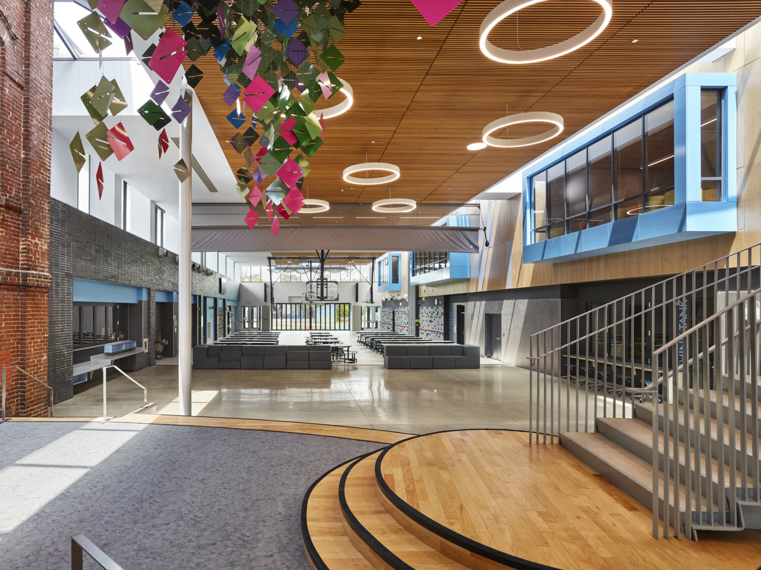 Double height atrium with exposed brick, left, and blue overhanging 2nd floor windows, right. Multicolor sculpture hangs left