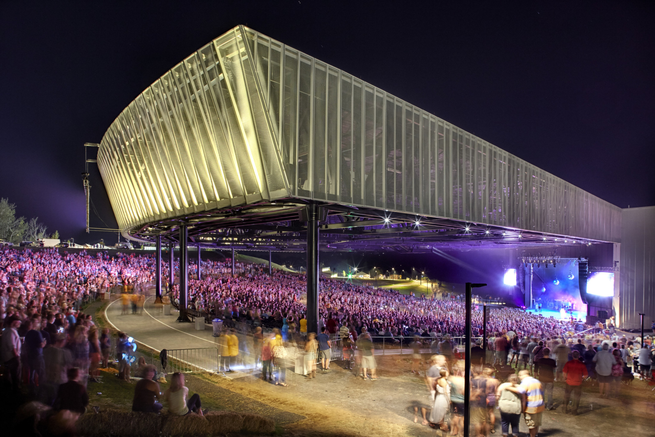 Corner view of crowd in partially covered St. Joseph Health Amphitheater at Lakeview at night while band performers on stage