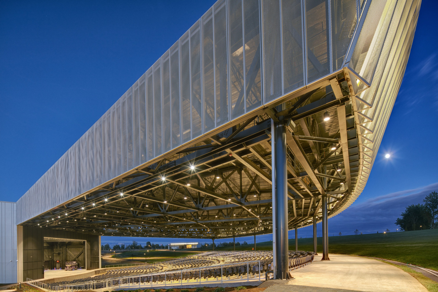 Amphitheater with lights in rafters viewed from front corner facing stage, showing ridges along fascia front