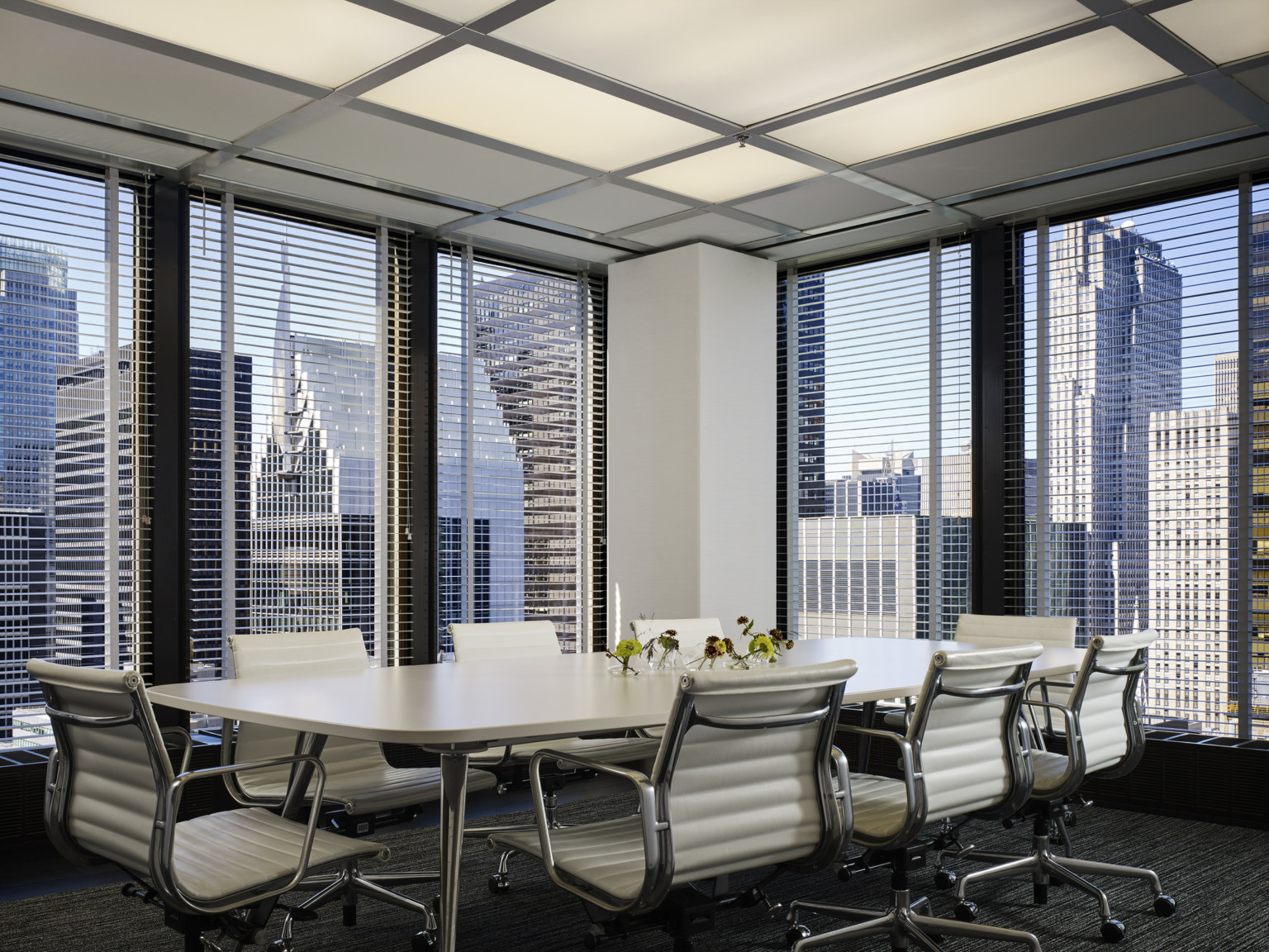 Corner conference room with floor to ceiling windows on both walls separated by white column. Long white table and chairs
