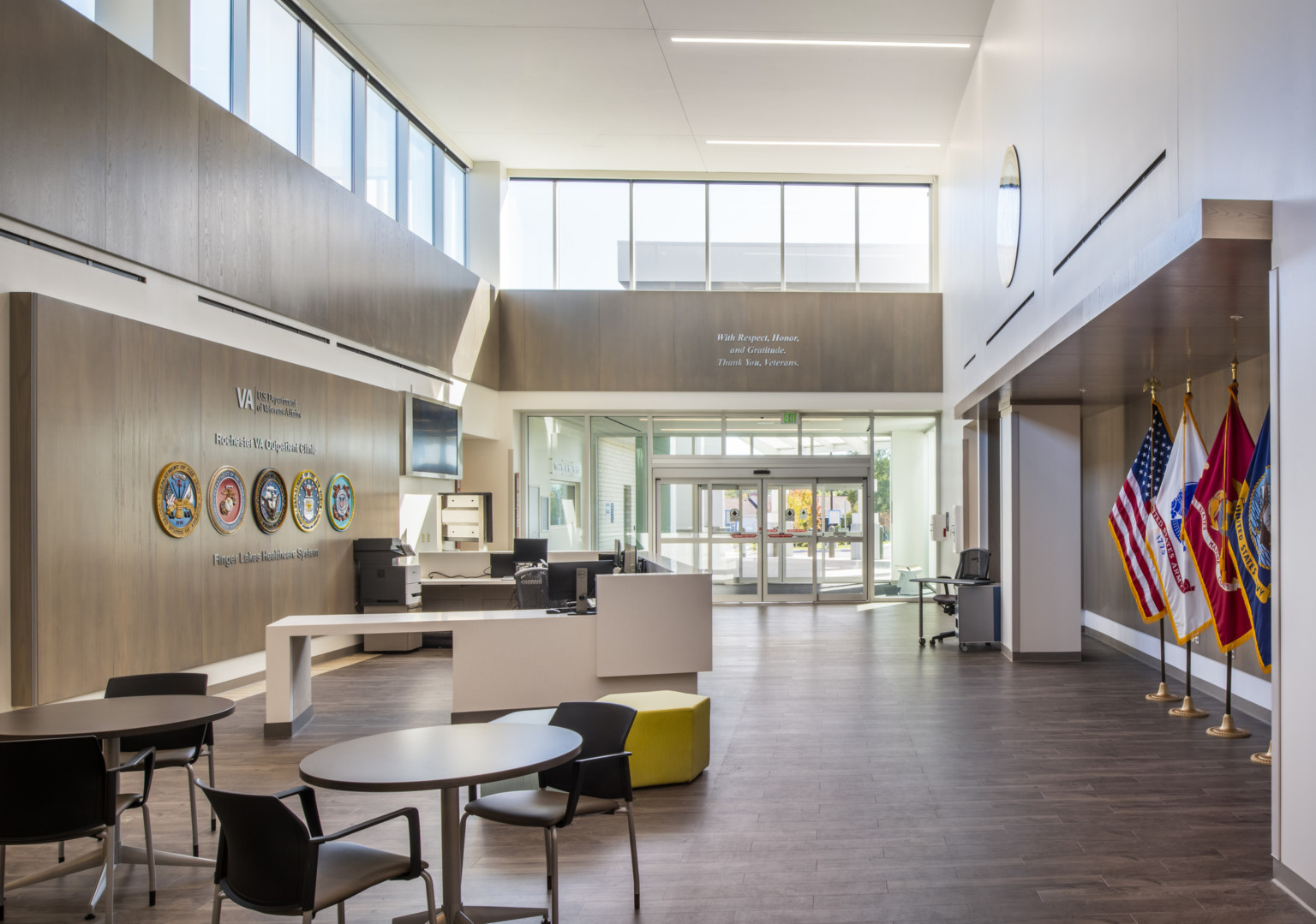 VA Outpatient Clinic lobby and reception, a white room with wood accents. Flags stand to the right, seals left behind desk