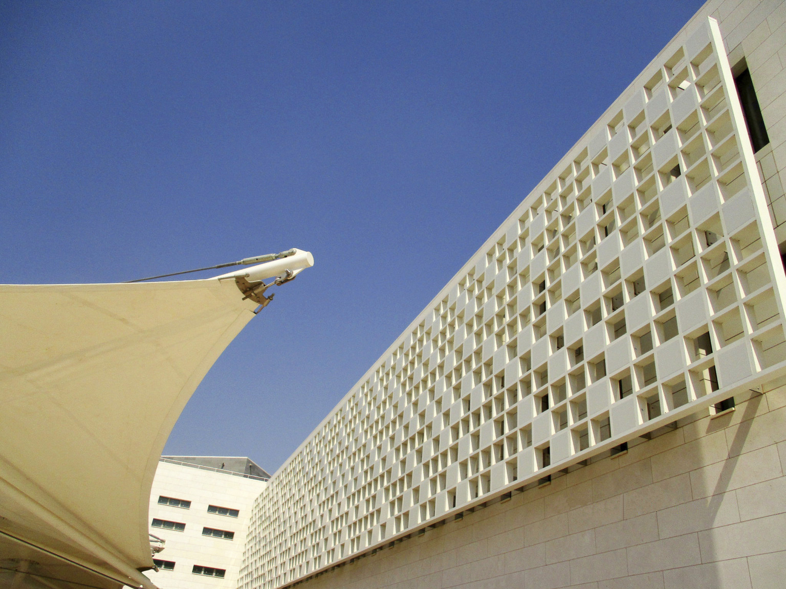 Closeup of white sun screen with squares of tile and space along the upper floors of the building.