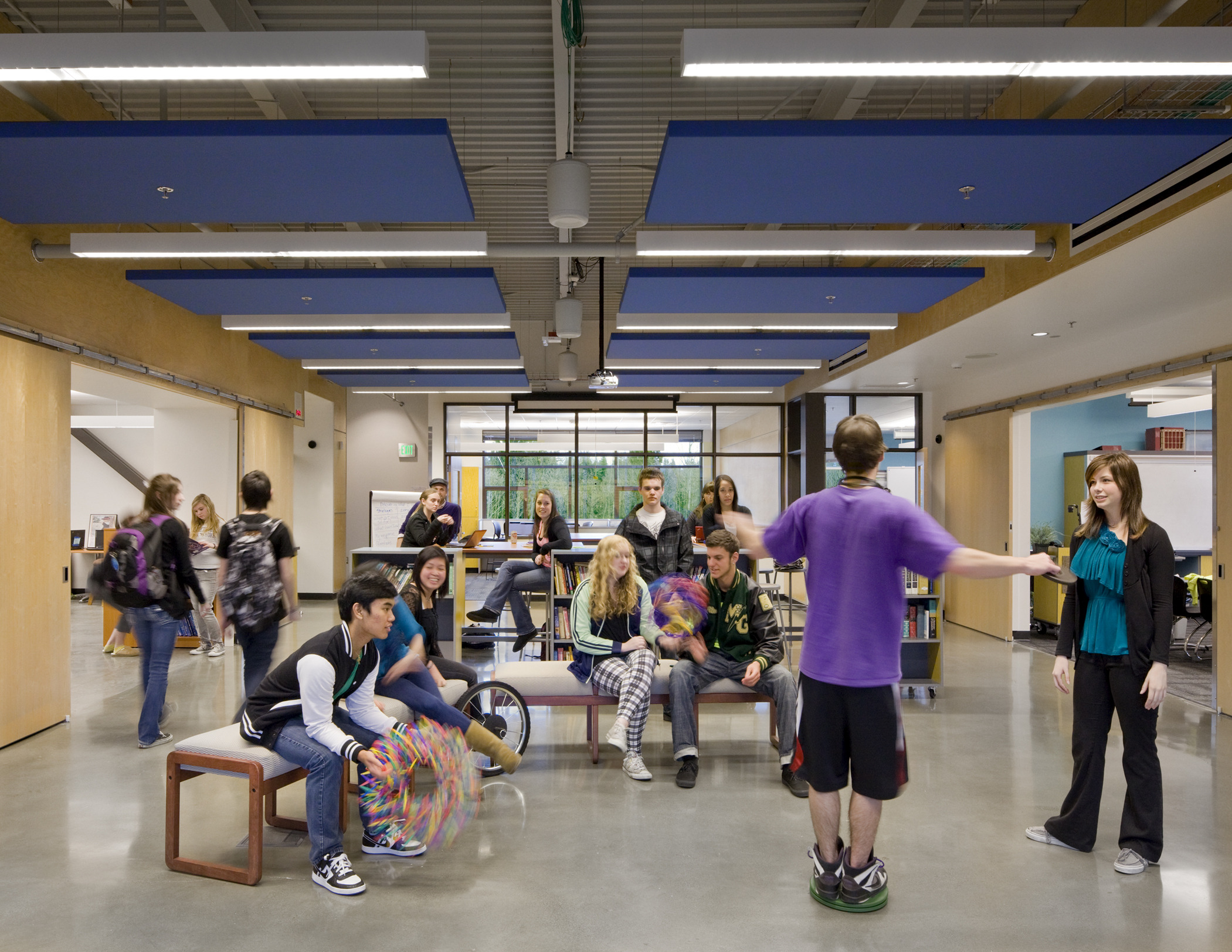 Benches in white hallway between classrooms with wood sliding double doors opened. Blue panel drop ceiling details and lights