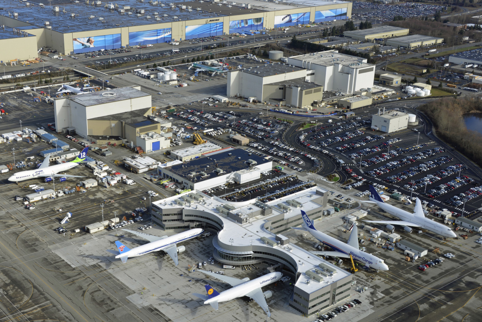 Boeing Partnership site aerial view. White building with rounded edge at front surrounded by planes and parking lots