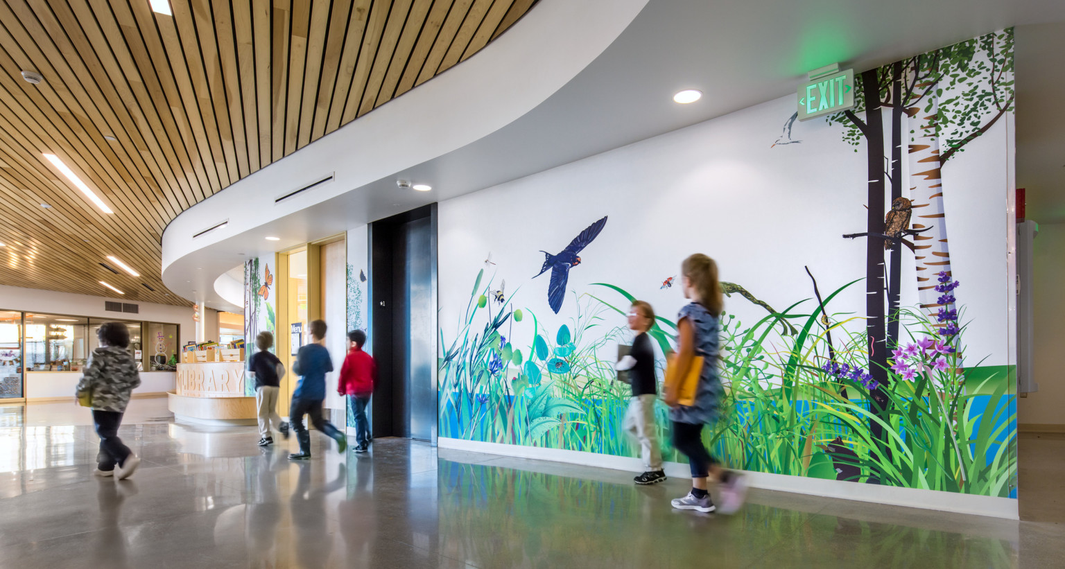 A curved hallway with wood panel ceiling and a mural along the wall of grass and animals. Wood desk curves with hall
