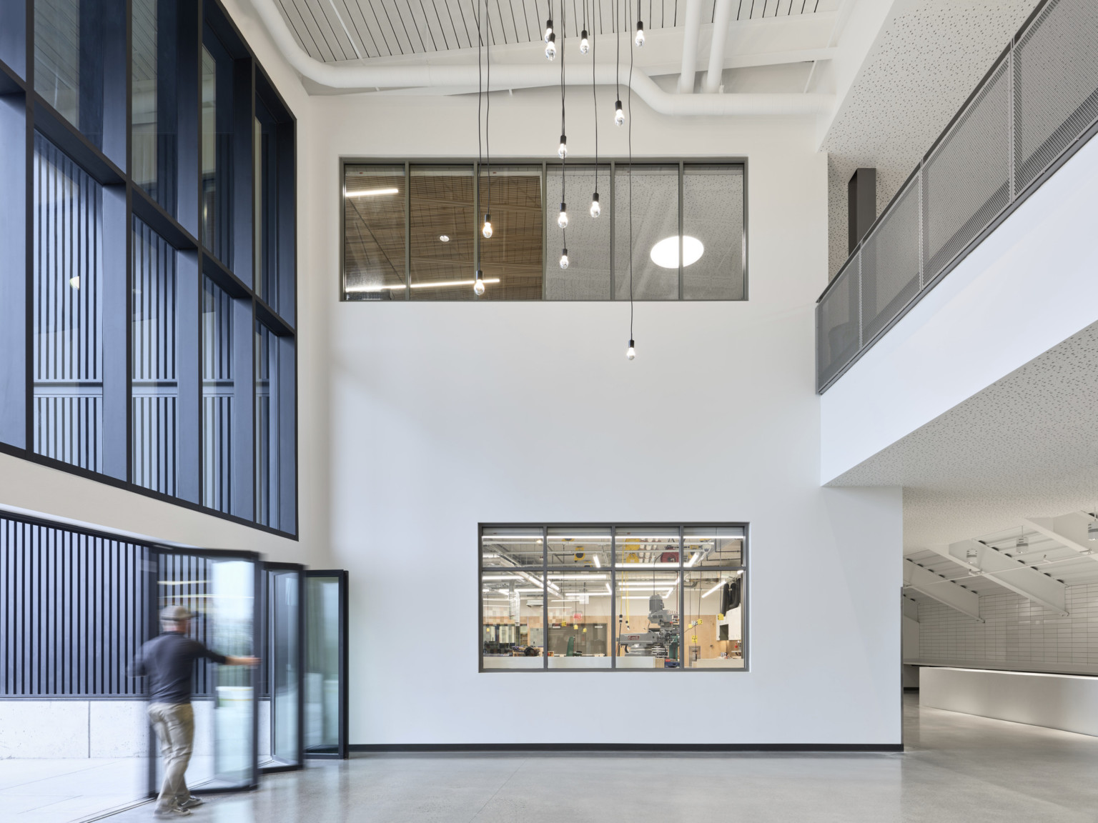 Interior view of wall folding in front of double height white wall with windows at each level. Lights hang from black cords