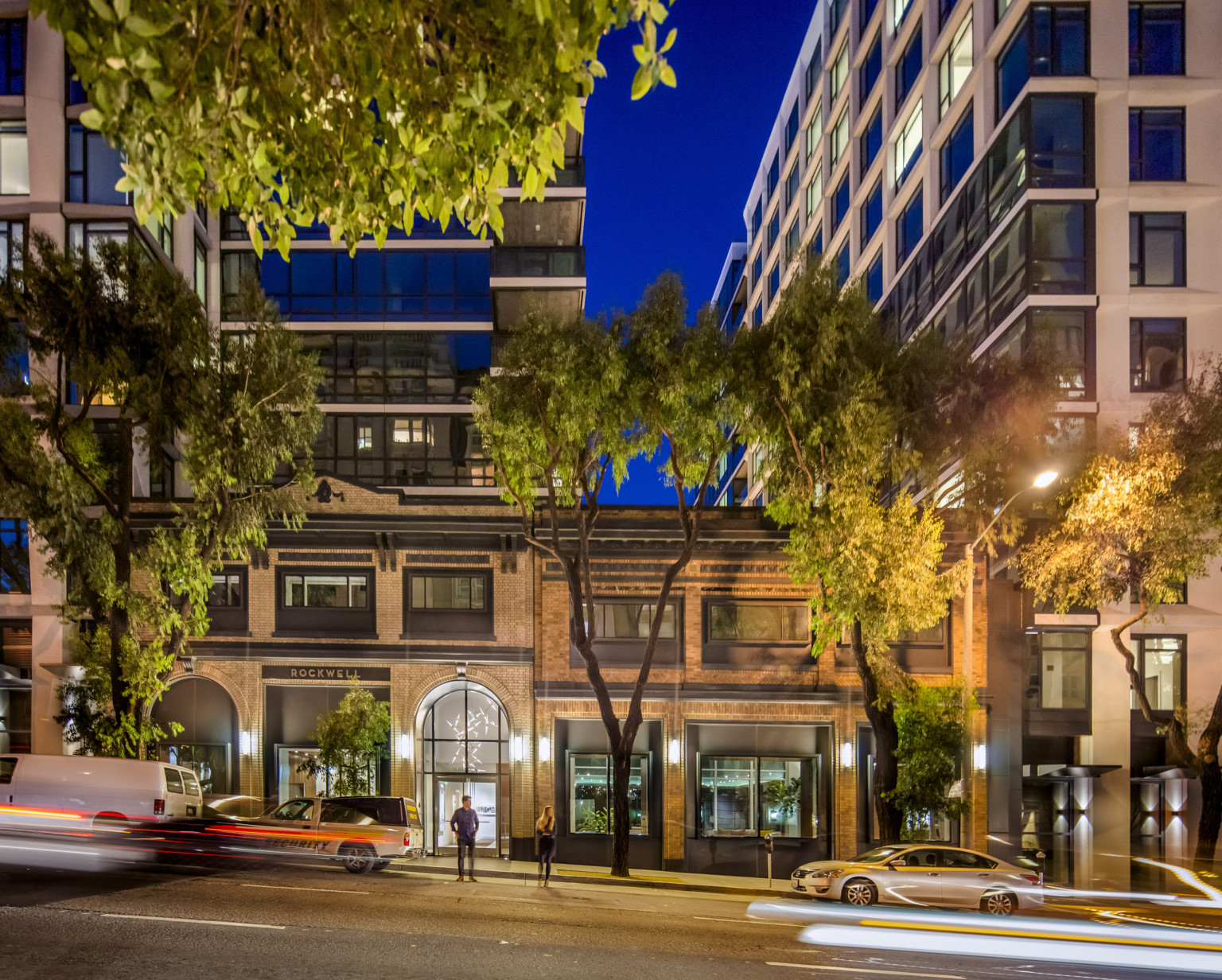 The adjacent brick building, labeled Rockwell, at night. Arched glass entry to white hall with sculptural hanging light