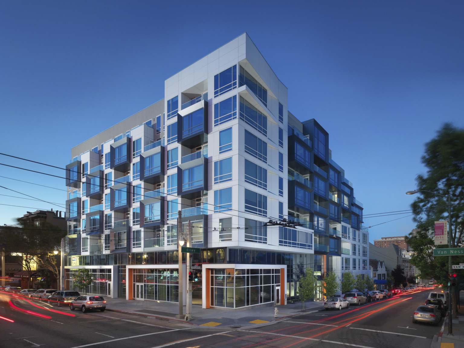 Corner view of building with large windows and black base below white wrapped facade upper levels and awning patterning wall Corner view of building with large windows and black base below white wrapped facade upper levels and awning patterning wall