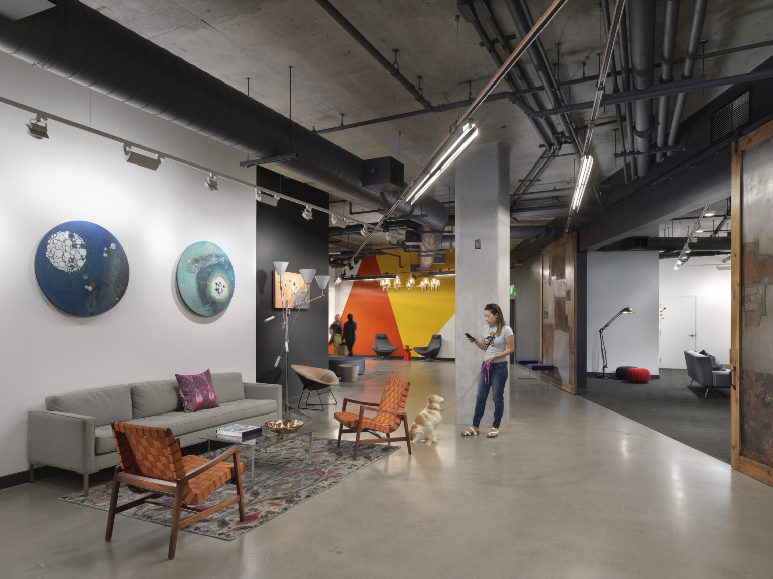 Seating in black and white room with wood sliding doors, right, to lounge. Orange and yellow geometric mural on far wall