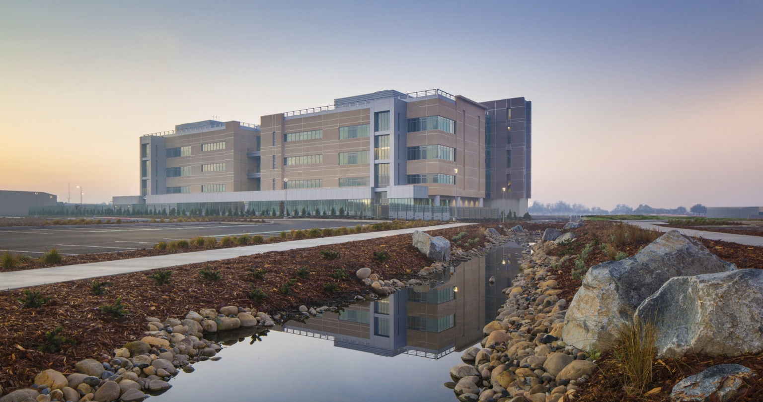 Kings County Courthouse exterior view. 4 story building with stone and glass facade from across parking, reflected in water