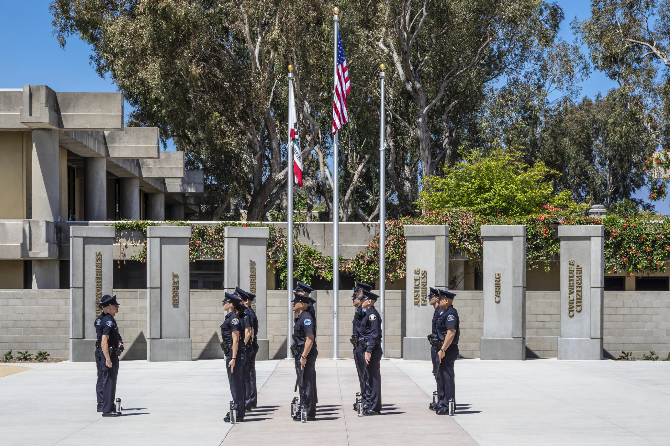 Police officers standing in formation outdoors next to flags and pillars at Golden West College, Regional Public Safety Training Center