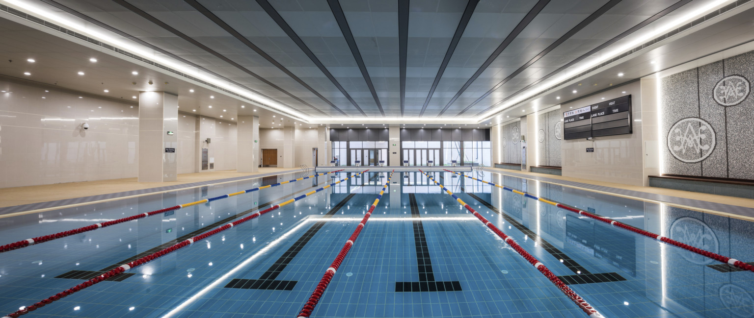 View looking down a lap pool to floor to ceiling windows. Recessed lighting lines the pool from above and tiled path on sides