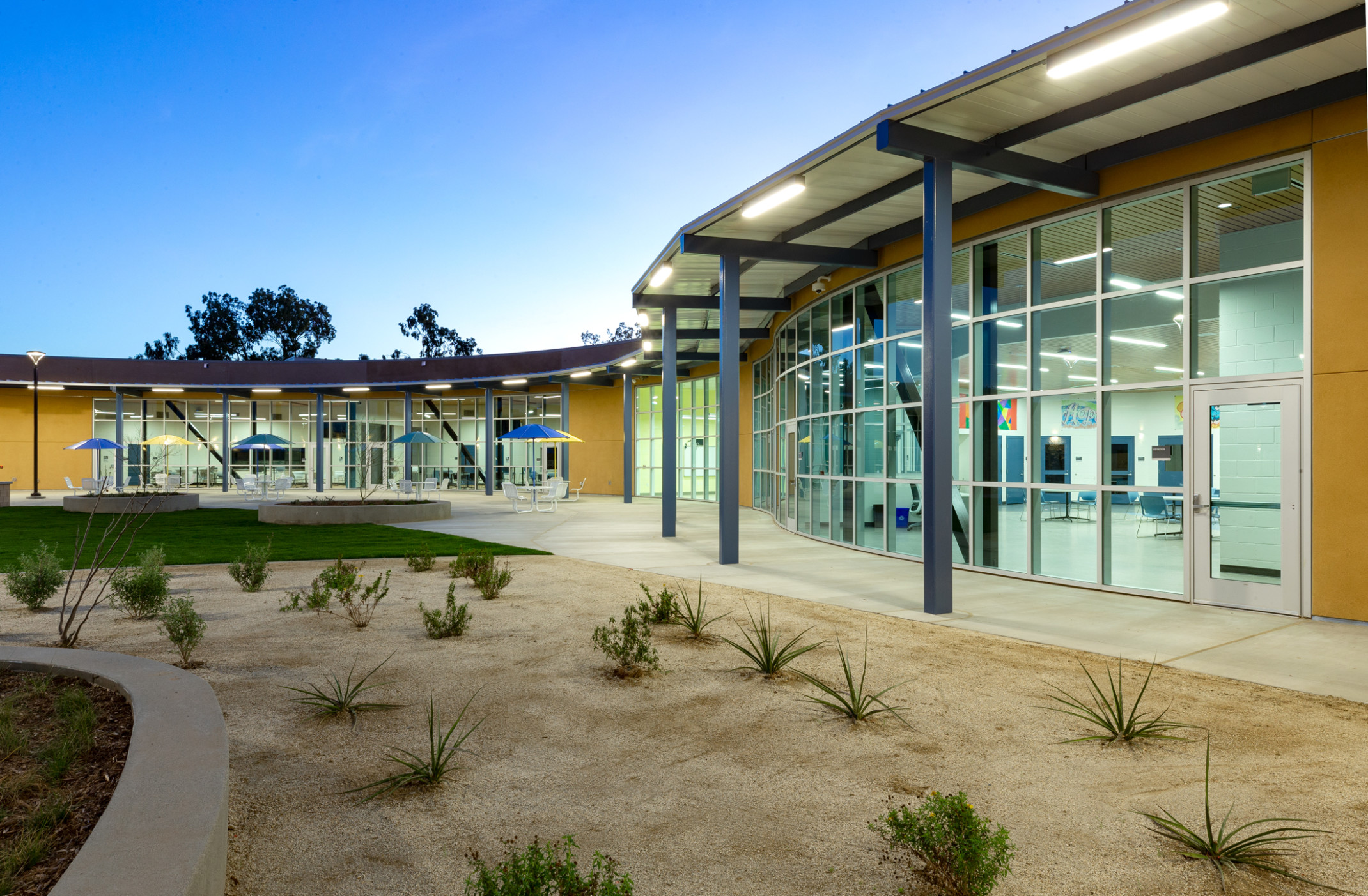 curved single story building with flat roof floor to ceiling glass facade with yellow panels. concrete paths in desertscape