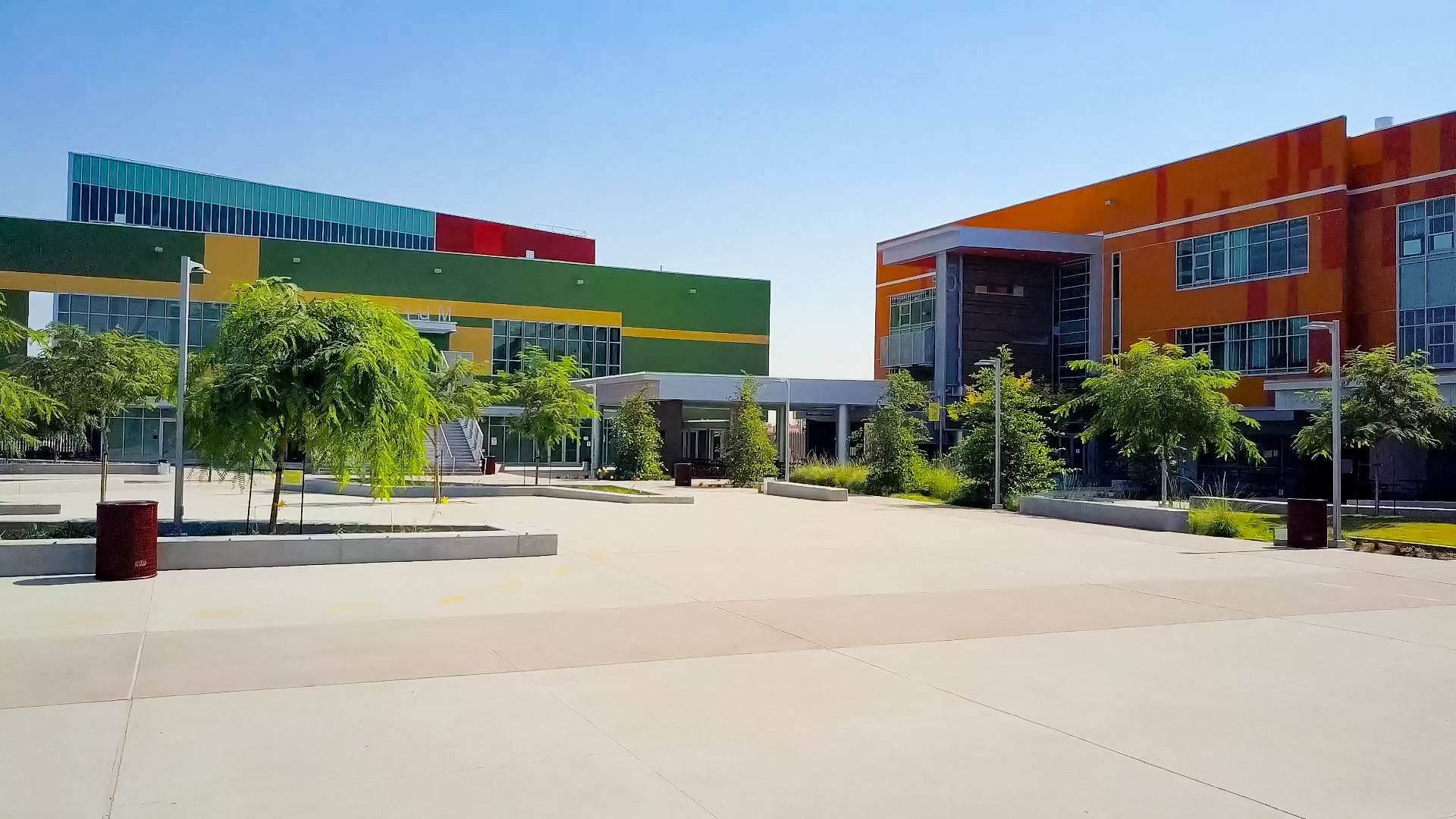 Standing in the center of a school campus surrounded by brightly colored buildings, palm trees, and seating areas Standing in the center of a school campus surrounded by brightly colored buildings, palm trees, and seating areas