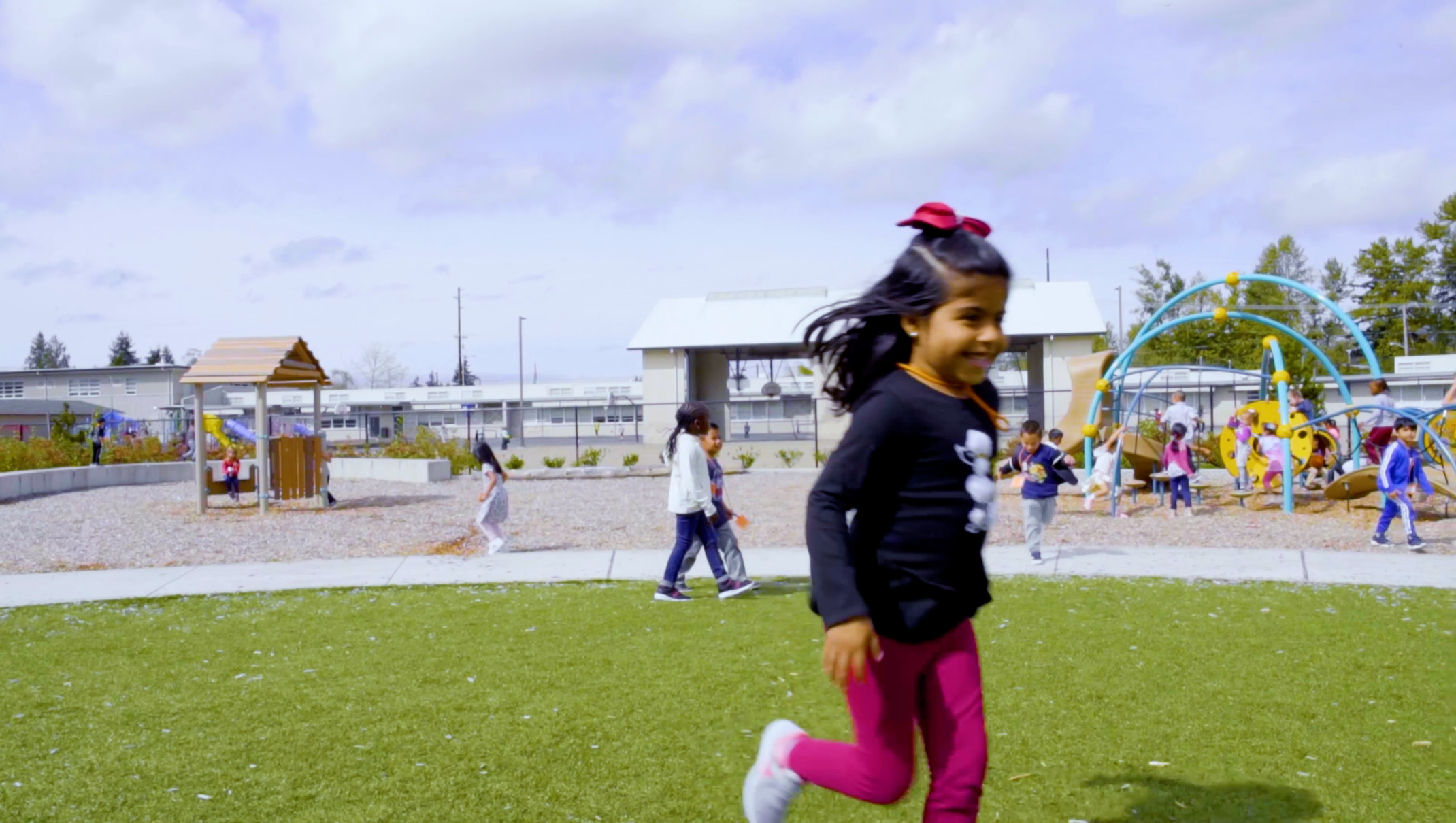 little girl running on an outdoor playground with a play gym in the background and areas for outdoor learning