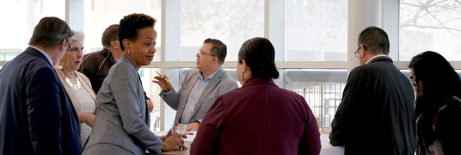 town and gown meeting with diverse stakeholders around a table in front of large windows with white seams