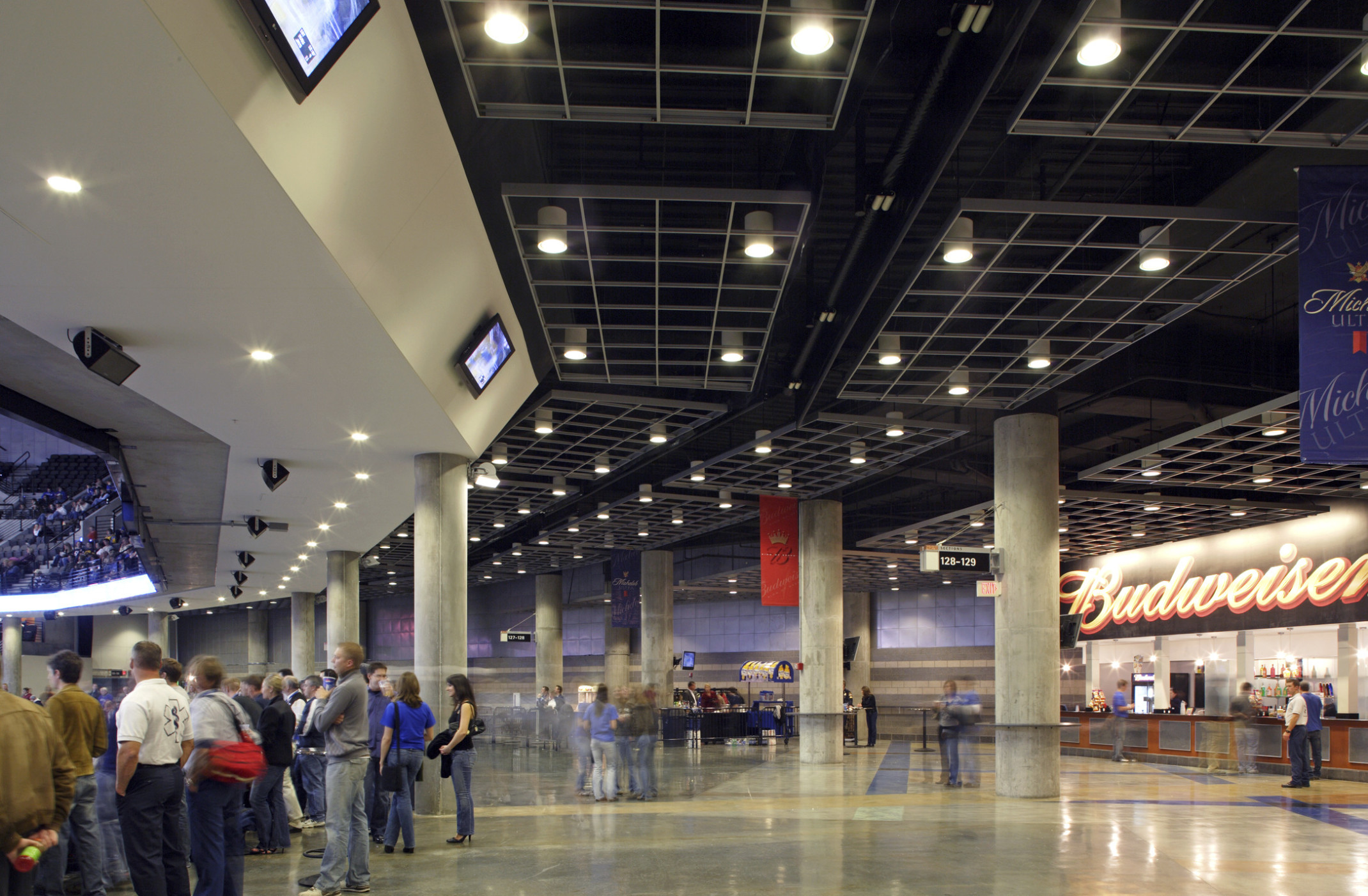 A hallway between levels with concession stand and tables to right. Black ceiling above has hanging grids supporting lighting