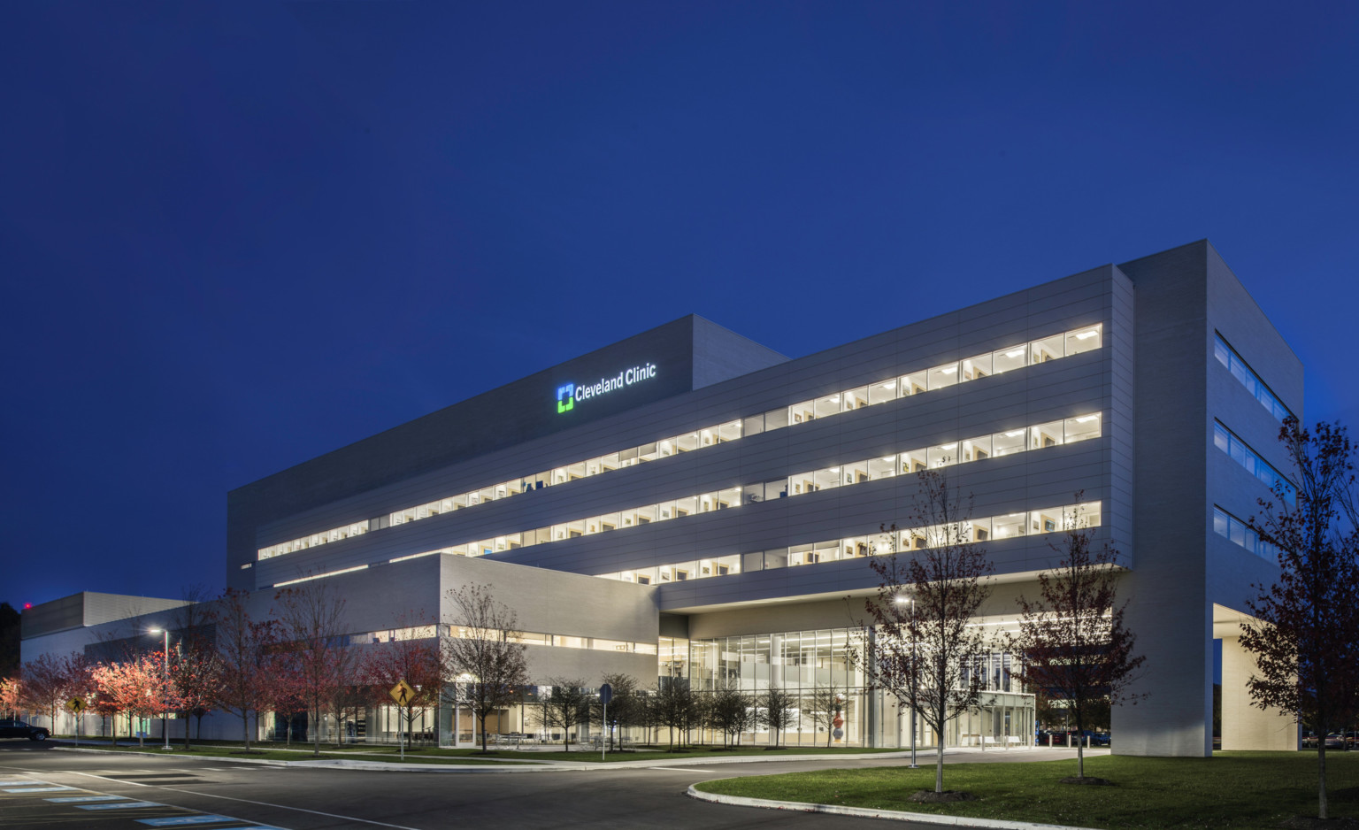 Cleveland Clinic Avon Inpatient Bed Tower illuminated at night seen from across the street facing drive up glass doors