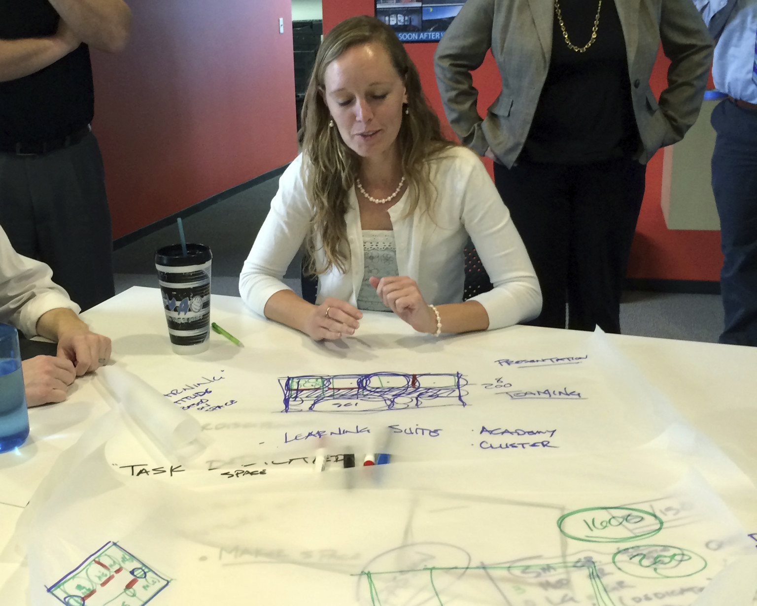 Woman sits at a table with sketch paper and markers