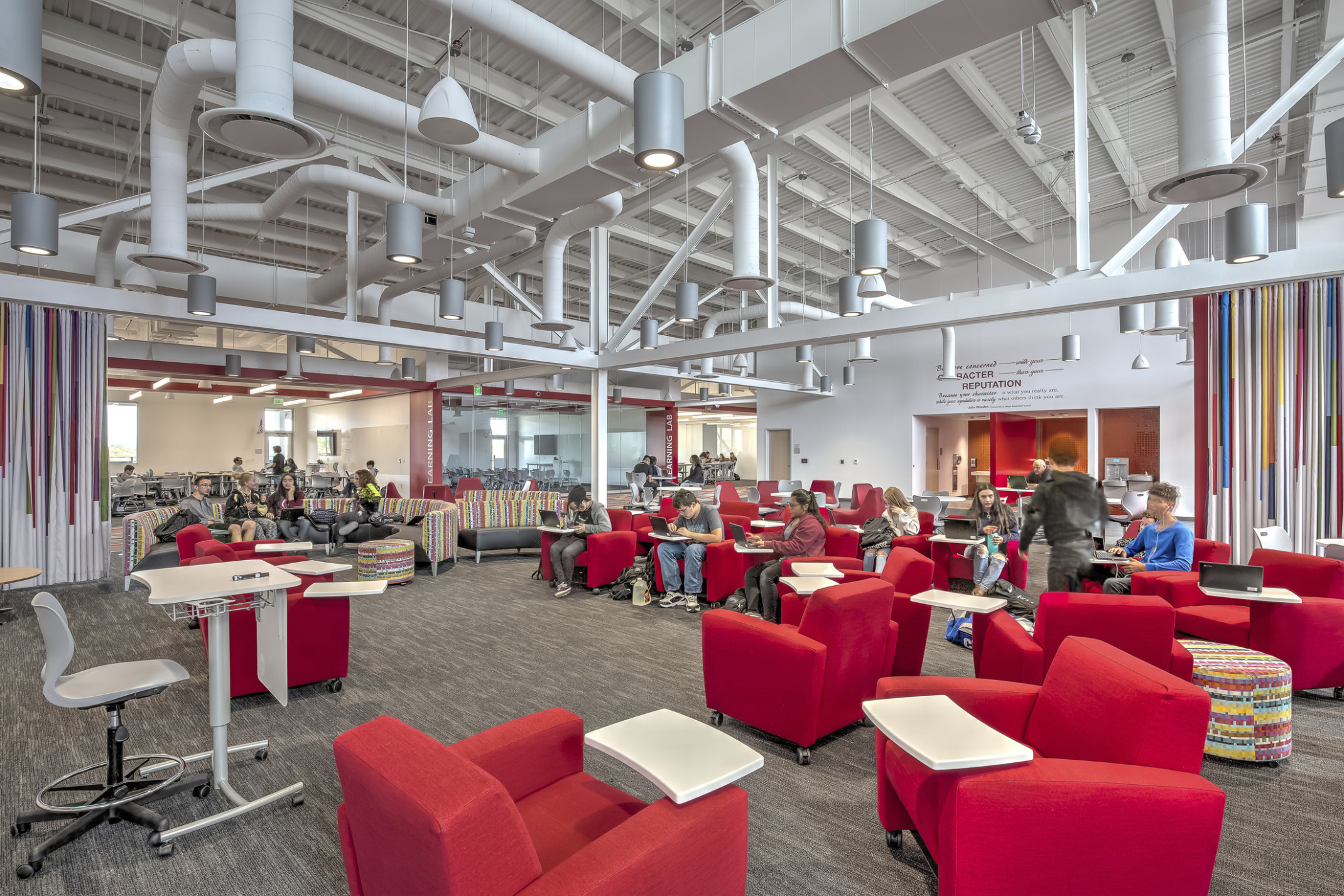 Large carpeted white room with red armchairs. Striped accent walls. Exposed ductwork and hanging pendant lights overhead