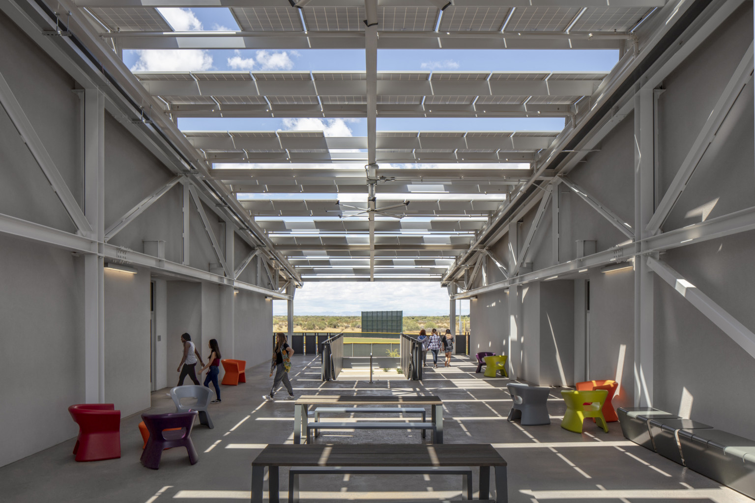 Solar panels stretch in rows between two white buildings, partially covering seating areas Solar panels stretch in rows between two white buildings, partially covering seating areas