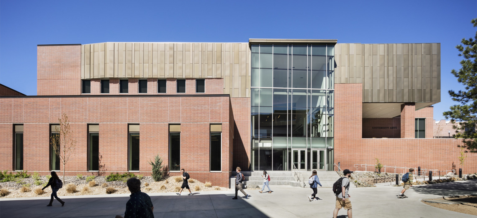 Exterior view of brick building with wood paneled accent at top level. A central glass atrium forms the lobby