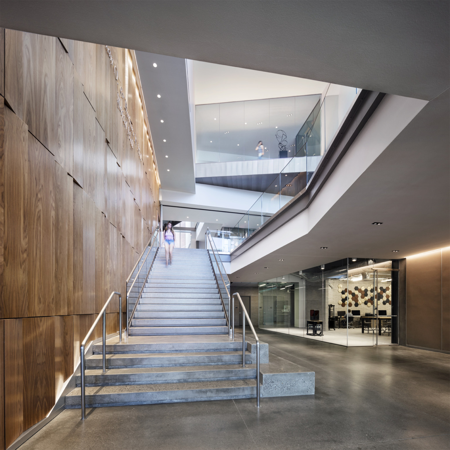 student walking down staircase next to textural wood wall with views behind of higher stories