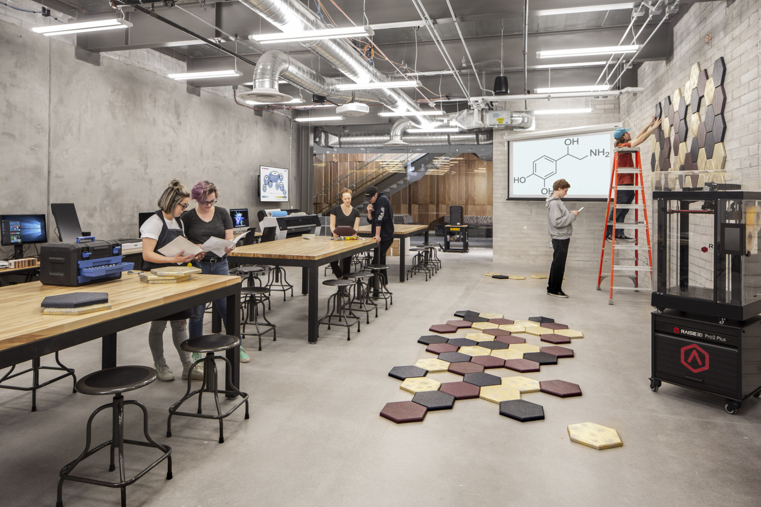 Students working with pentagon pieces in lab with long tables, computers, printers, and stools