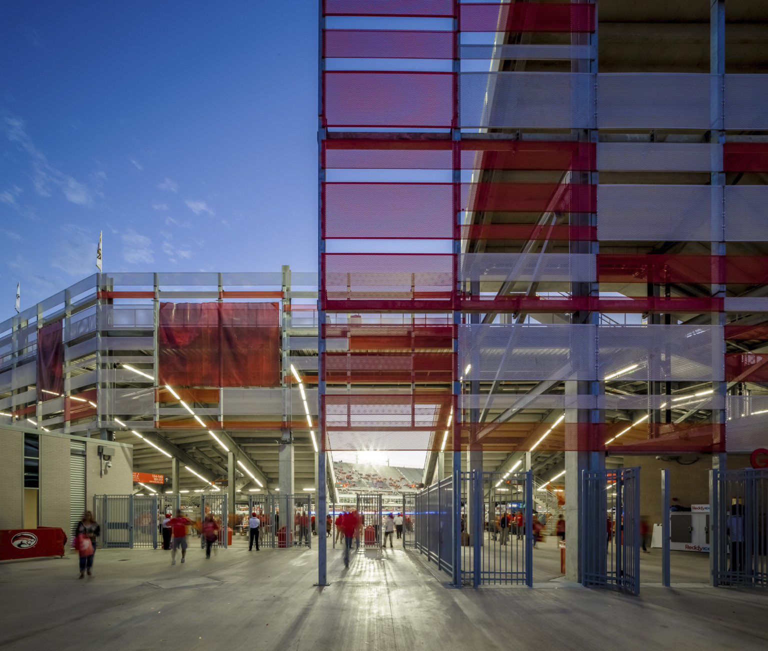 Closeup of perforated red and white metal panels of sunscreen facade around a gated stadium entrance