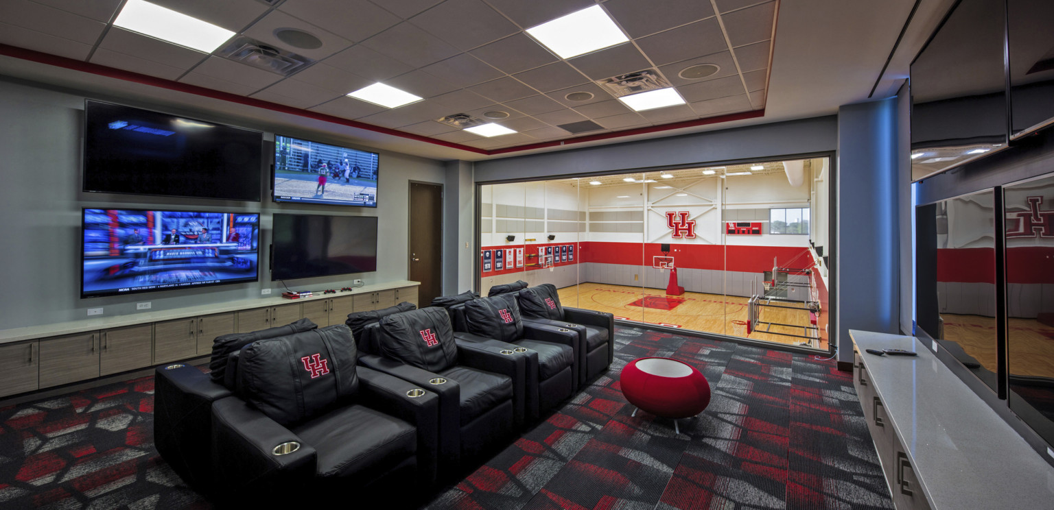 2 lines of armchairs face opposite walls with multiple screens. Far wall is floor to ceiling windows, basketball court below