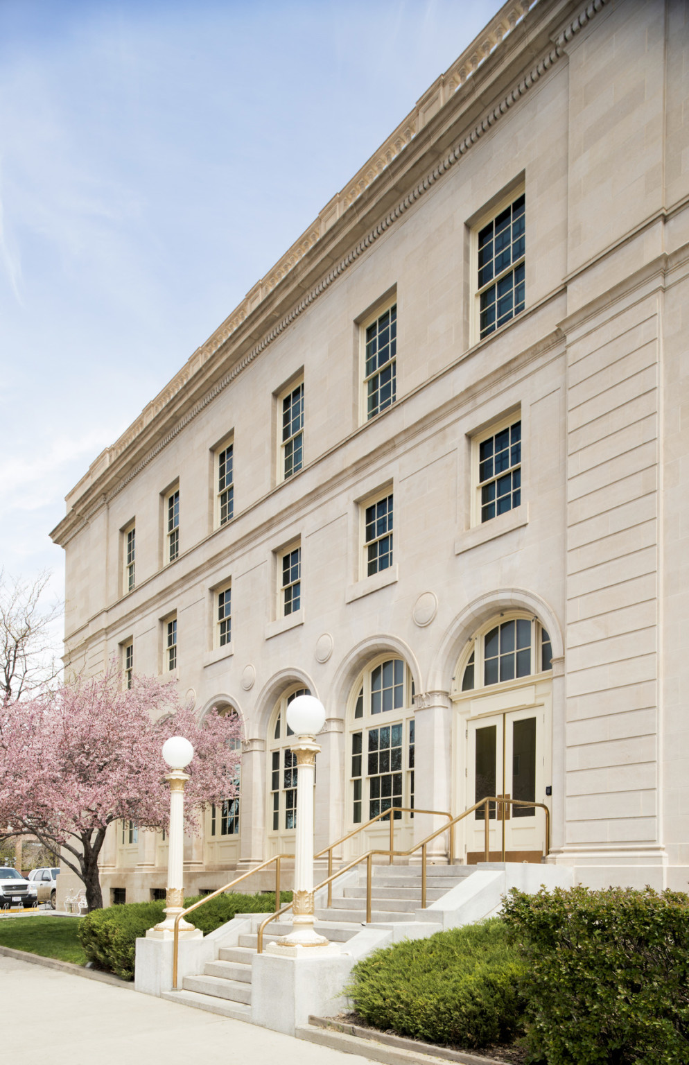 Exterior of entry with pillared arches around door and windows. Corinthian columns support rounded street lights by the steps