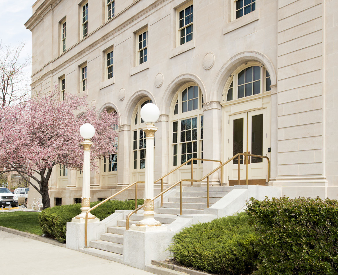 Exterior of entry with pillared arches around door and windows. Corinthian columns support rounded street lights by the steps