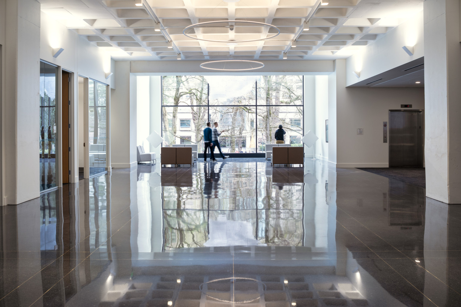 Interior hall with seating area and round hanging lights ending at double height windows, portland building renovation, restoration, postmodern architecture, michael graves architecture