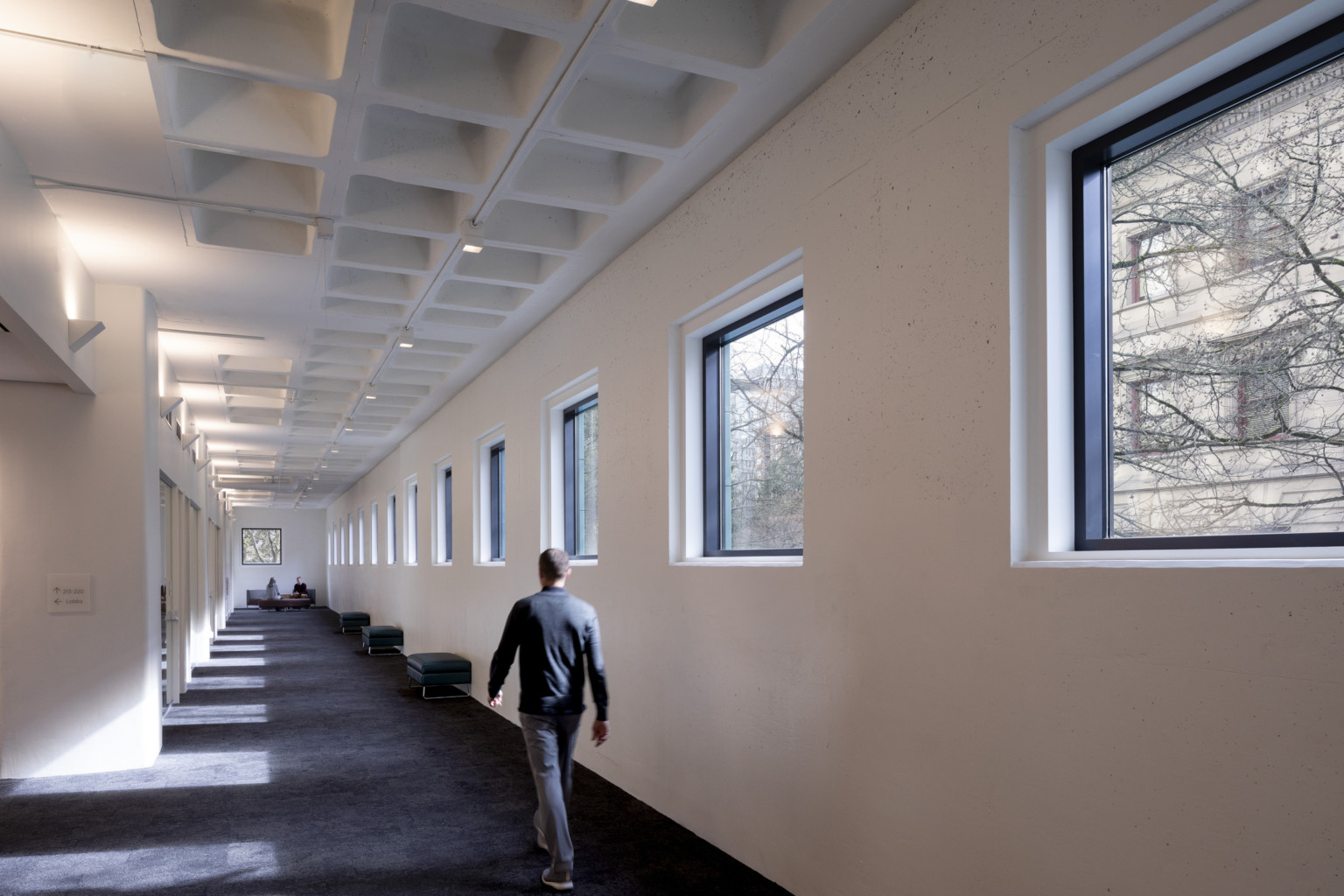 Tall white waffle slab ceiling over a perimeter corridor lined with square windows