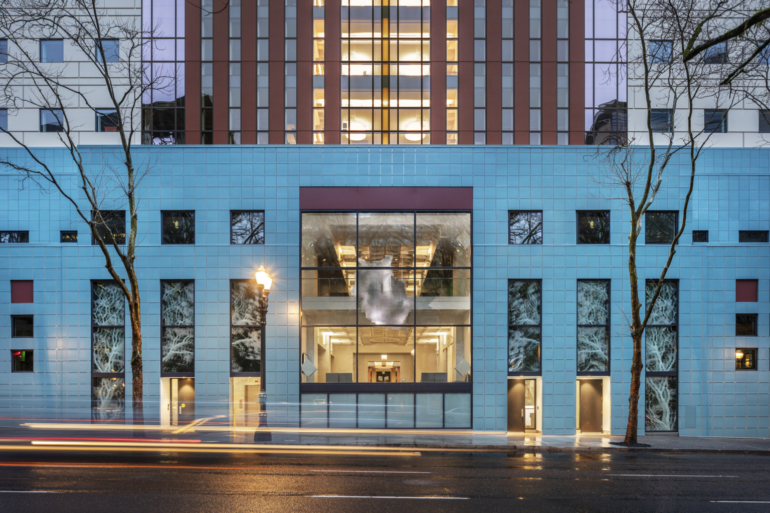 Exterior view at night of illuminated Portland Building with square window panels looking in to hung abstract art in atrium