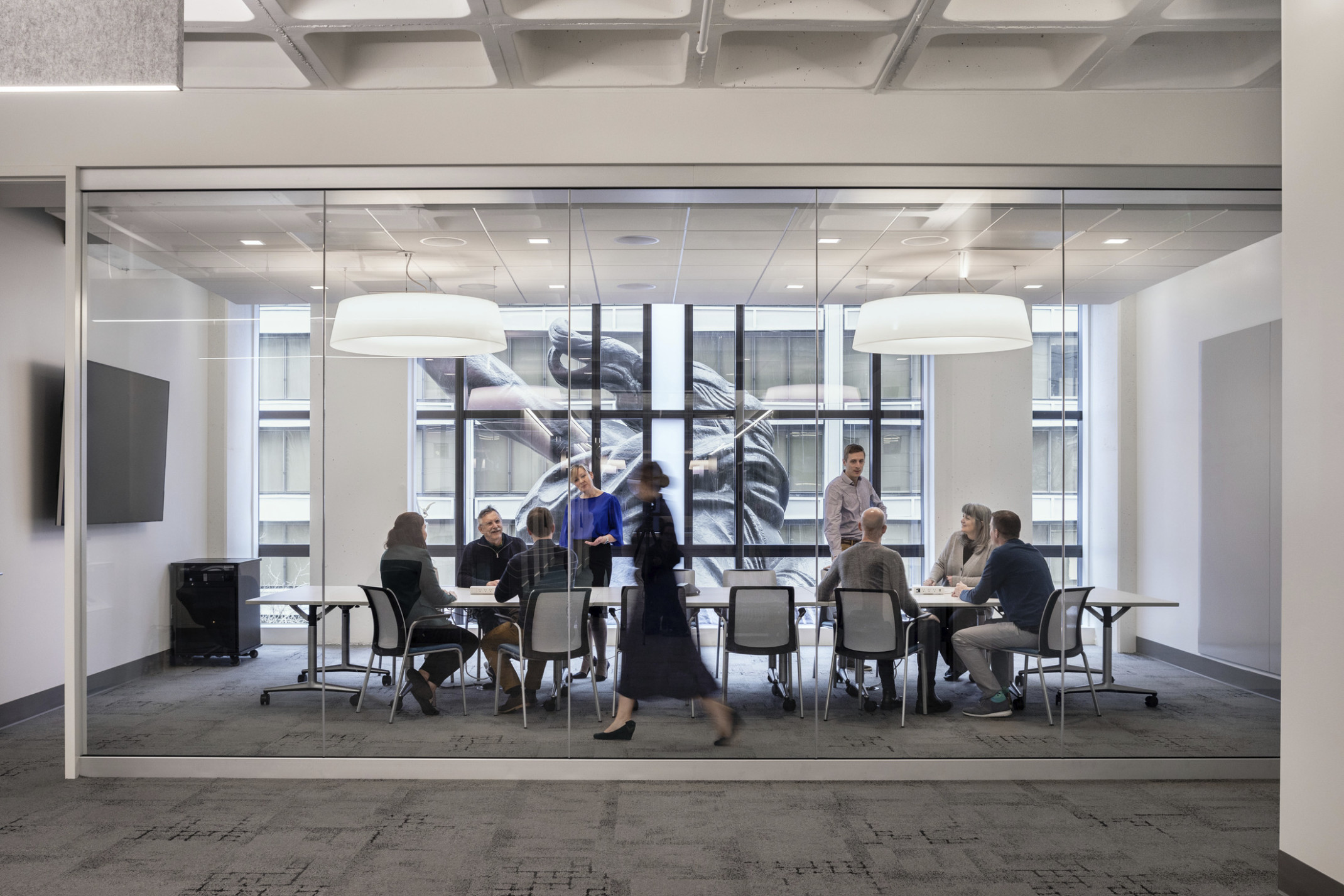 A conference room with glass wall into hallway has floor to ceiling windows looking onto the back of the Portlandia sculpture
