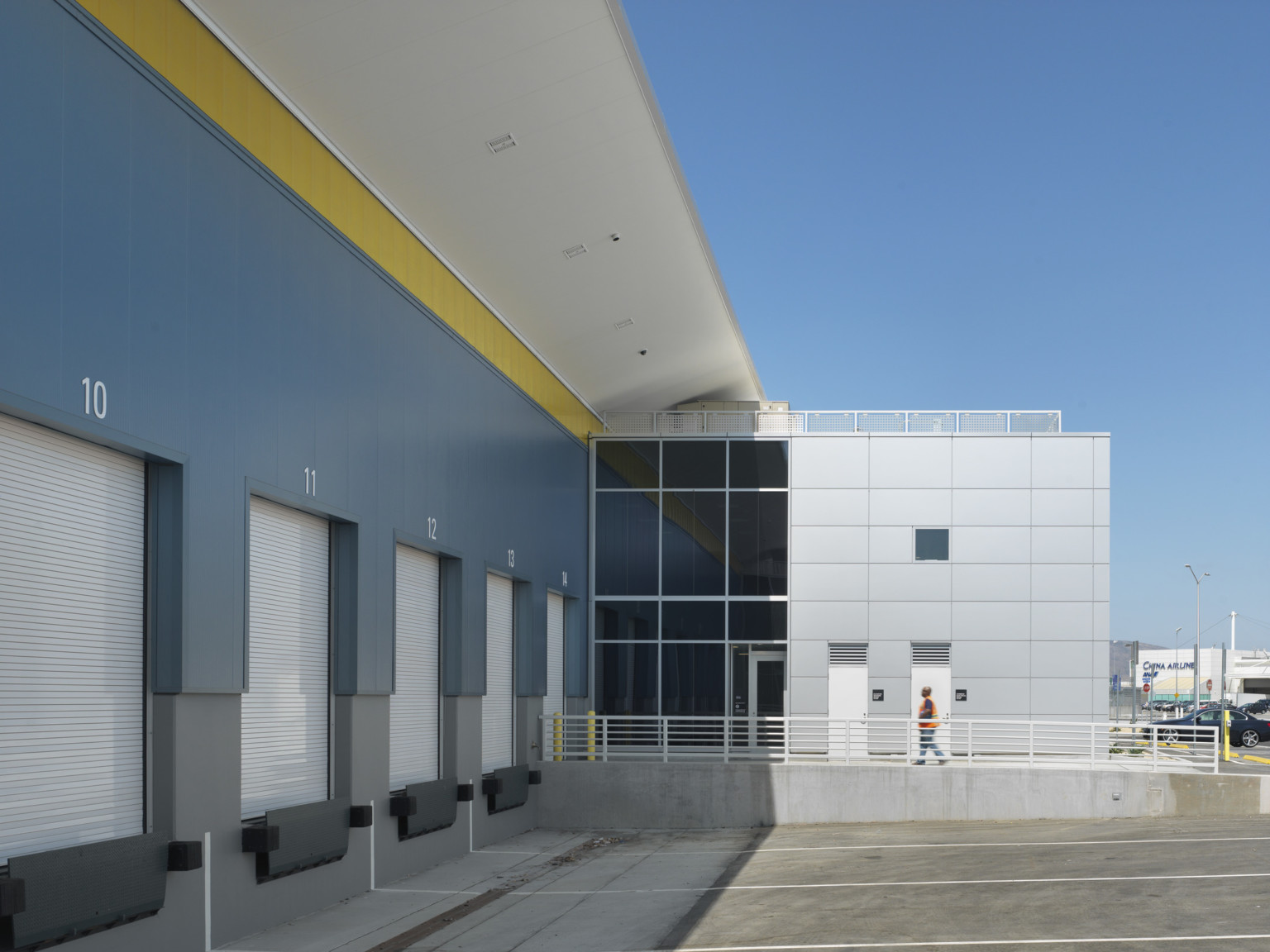 White numbered loading doors with parking spaces in front of a blue wall with yellow trim along white roof