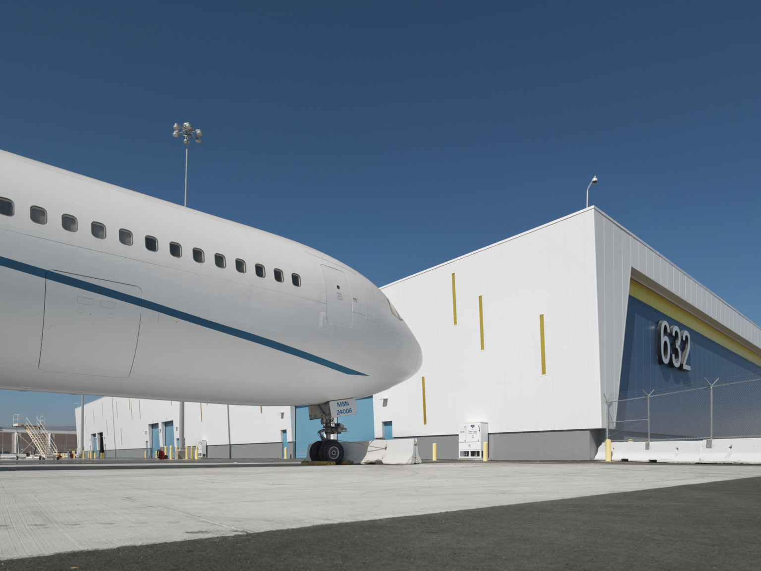 Corner view of blue and yellow building with white wrapped facade with yellow accents on side facing plane with loading doors Corner view of blue and yellow building with white wrapped facade with yellow accents on side facing plane with loading doors