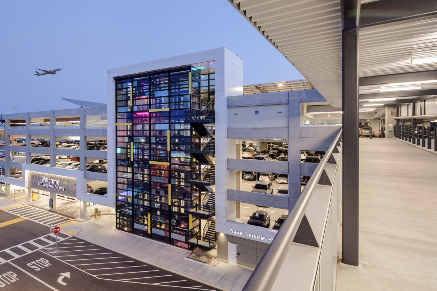 View from skywalk over road connecting to garage at 5th floor. Entrance to left, past glass tower. Plane flying above