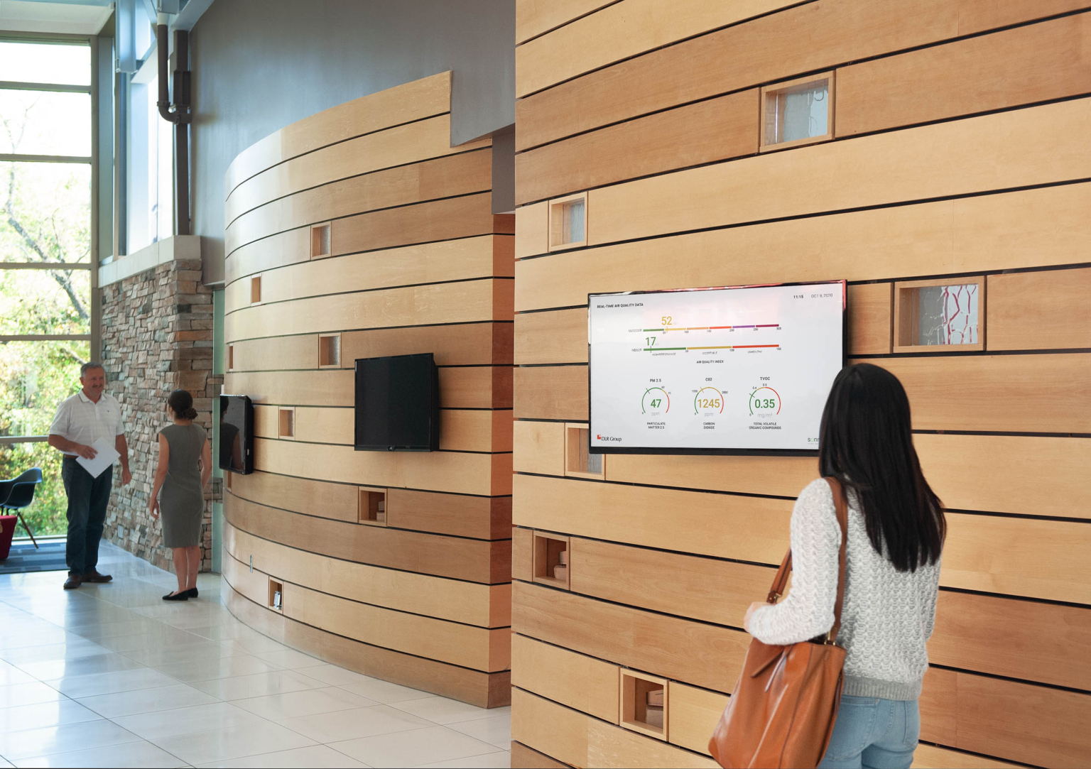 person in office building looking at tv screen on wood panel lobby wall displaying current air quality data on it