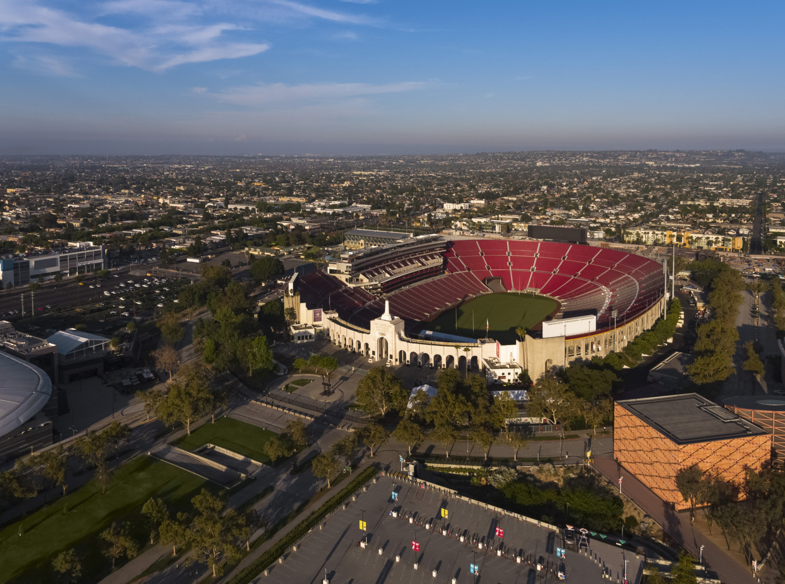 Aerial view of empty coliseum from above the parking lot facing entry concourse. Red seats in bowl, concrete arches at front