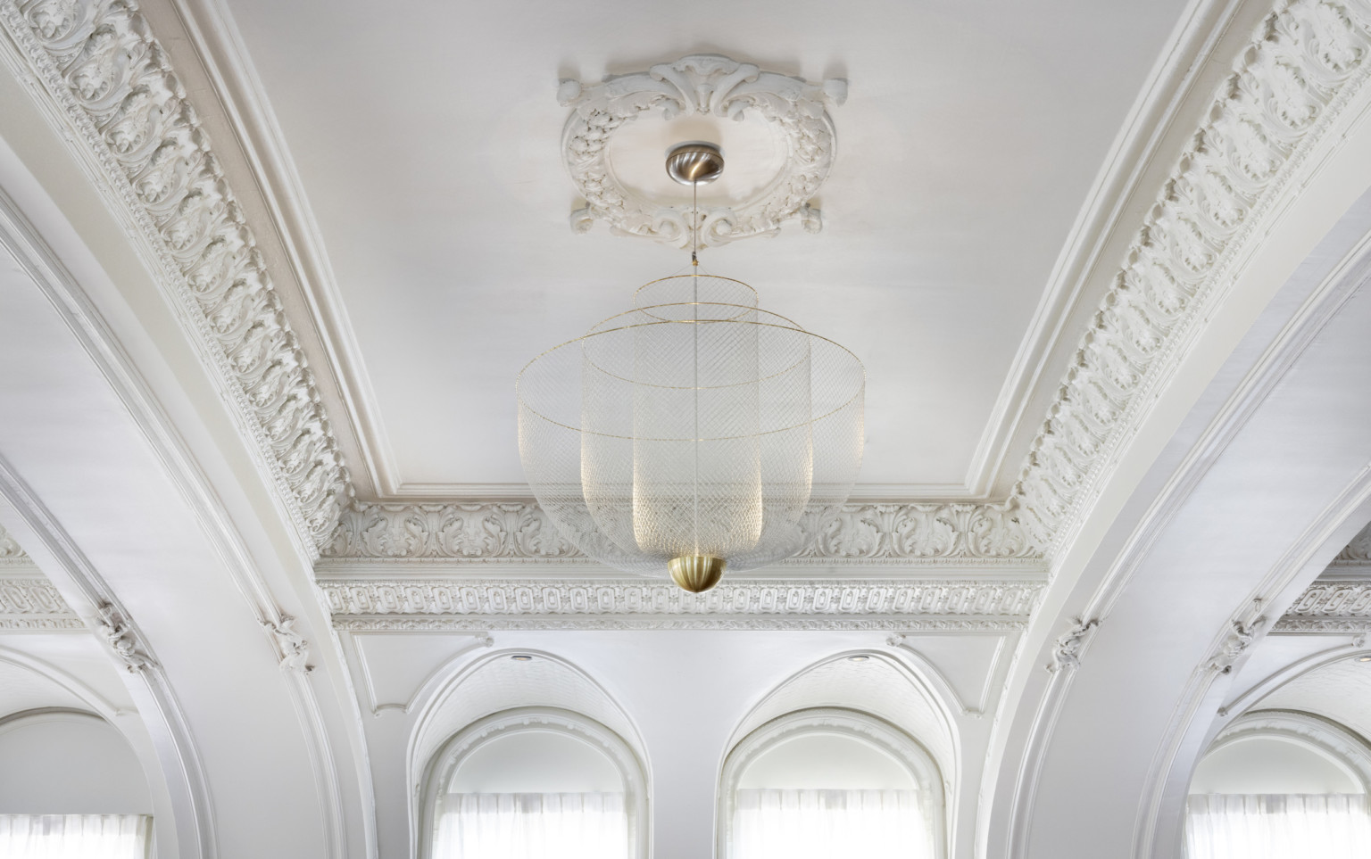 Close up view of hanging light fixture with 3 fishnet bowls which layer shorter and wider from the center, with gold rims