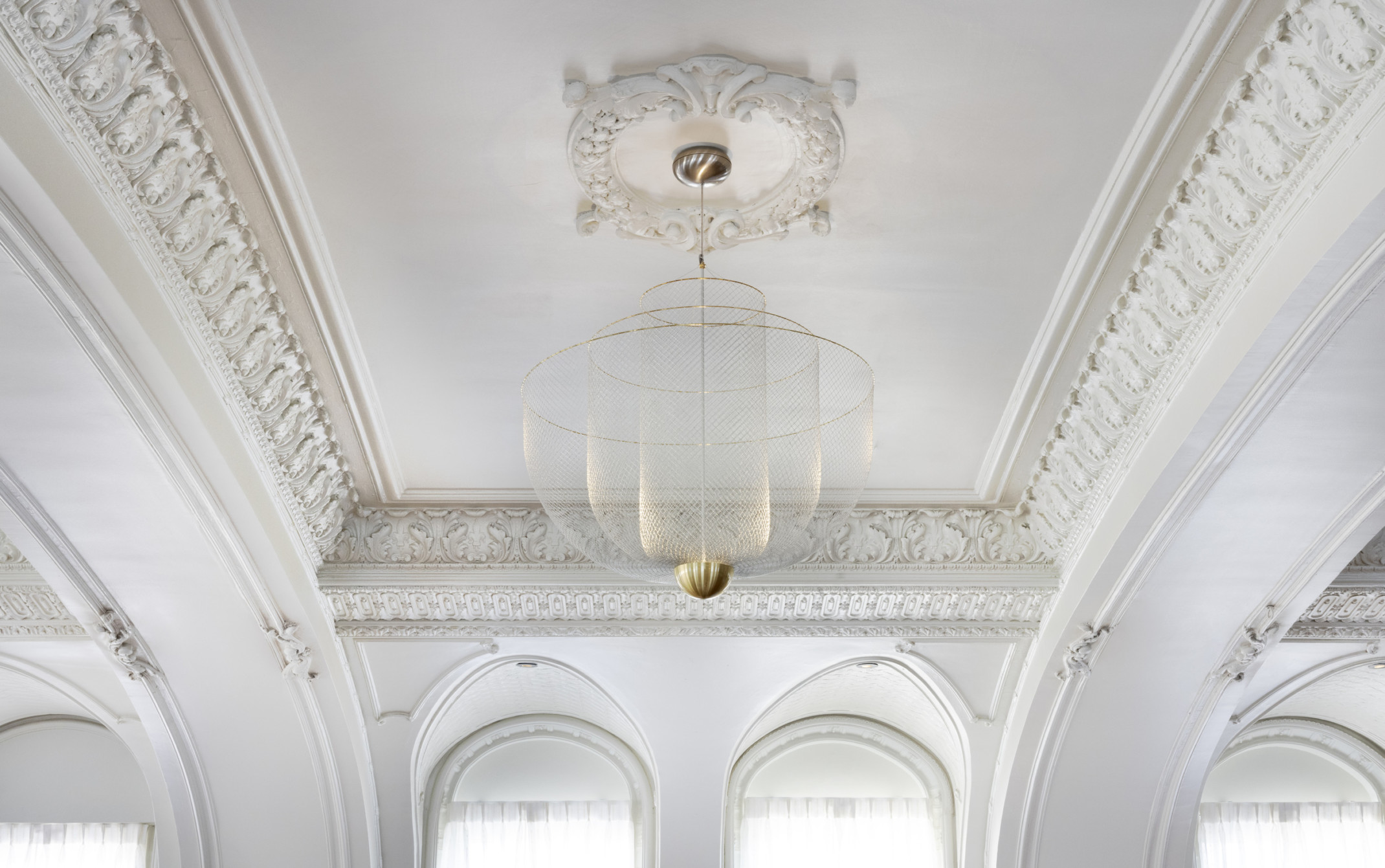 Close up view of hanging light fixture with 3 fishnet bowls which layer shorter and wider from the center, with gold rims