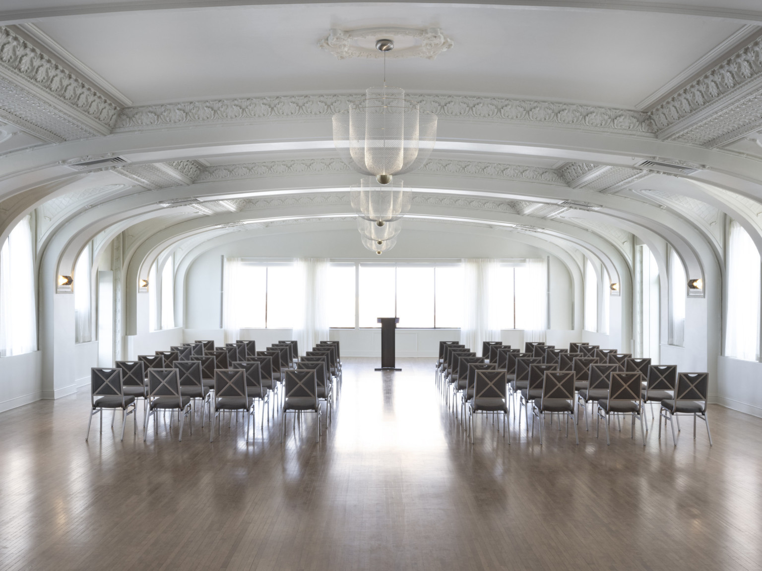 White arched room with recessed ceiling details with molded borders. Chandelier lighting down the center of the room