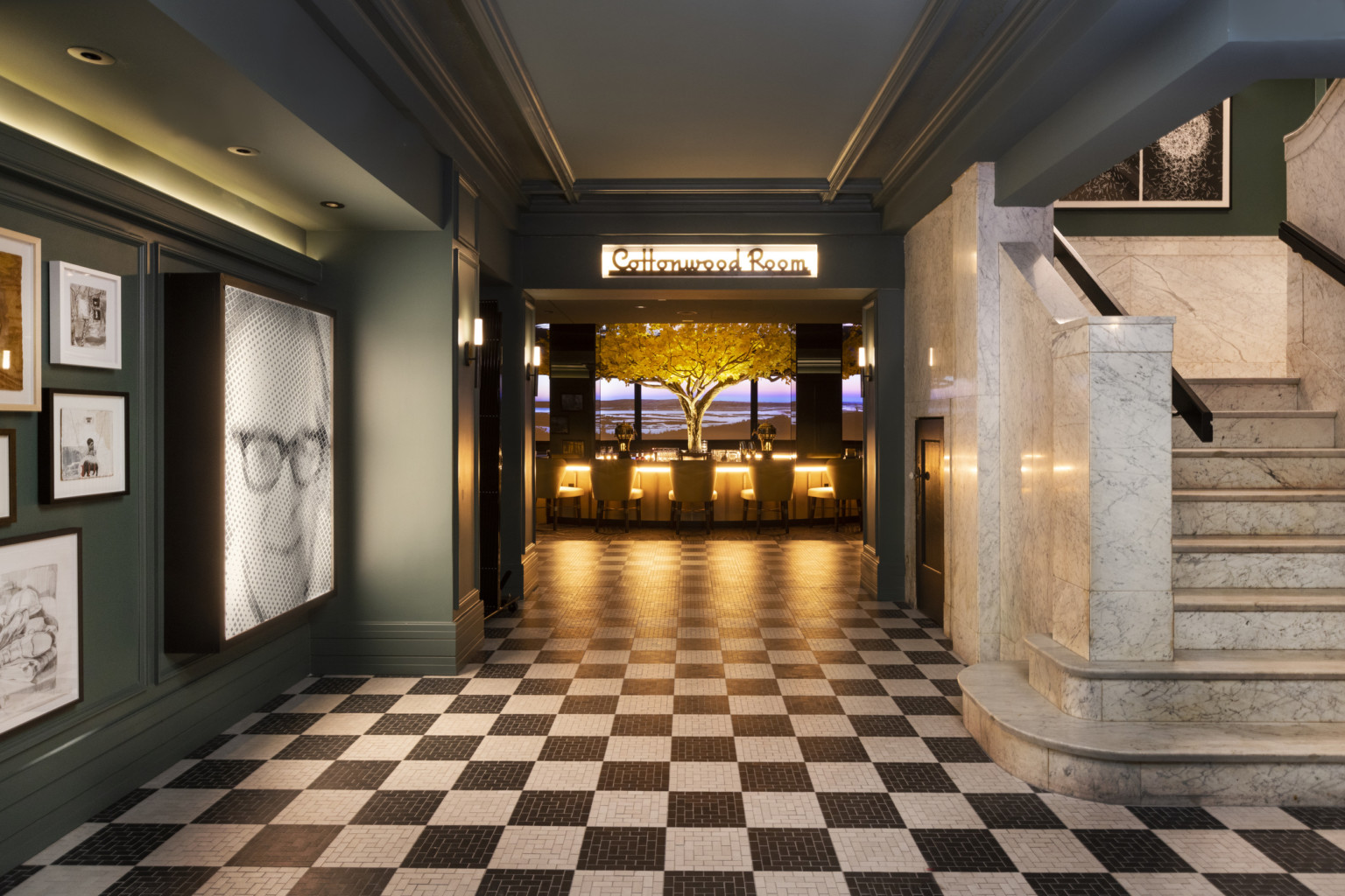 Black and white tiled entry to double doors of the Cottonwood Room, bar illuminated in the next room with yellow tree center