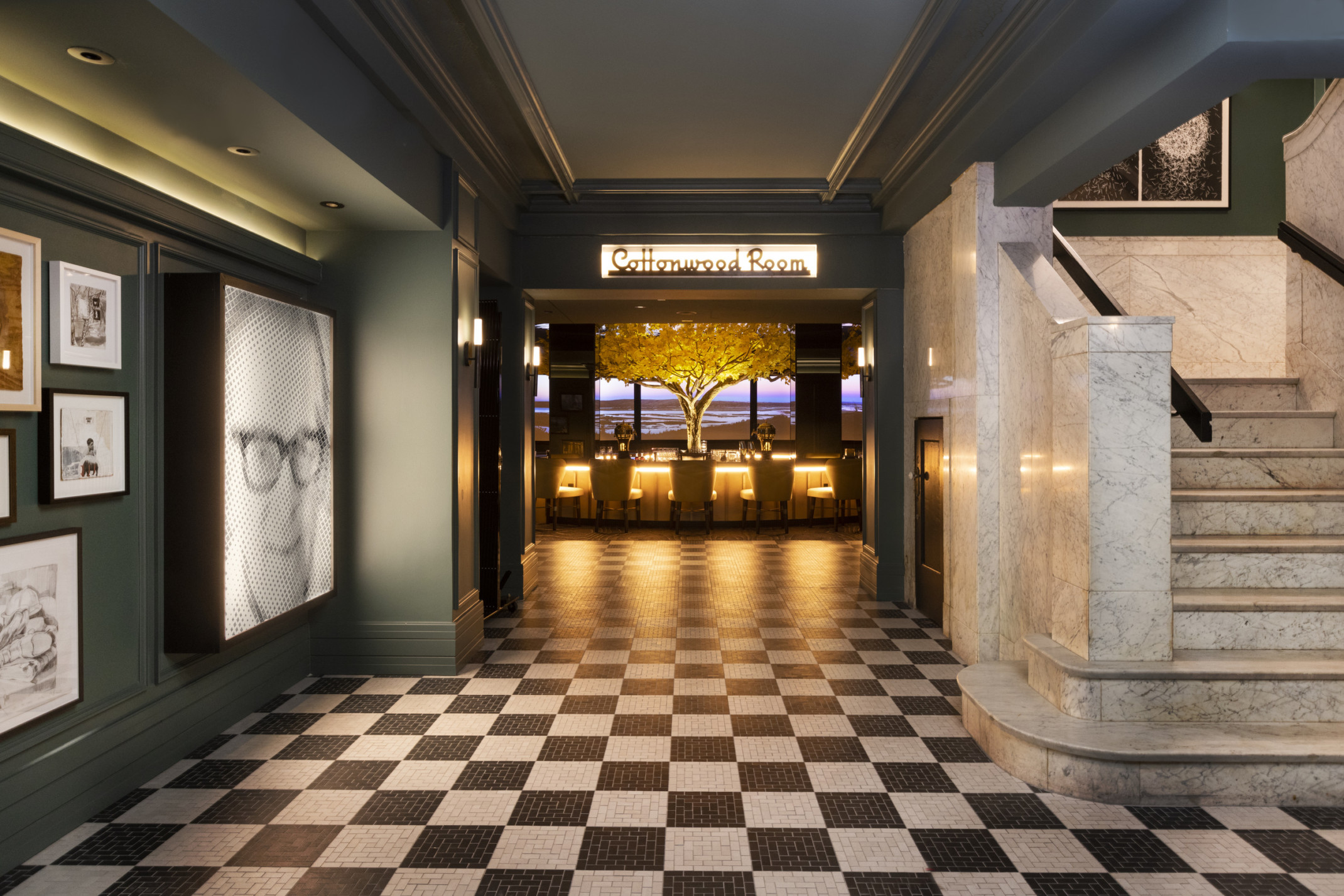 Black and white tiled entry to double doors of the Cottonwood Room, bar illuminated in the next room with yellow tree center