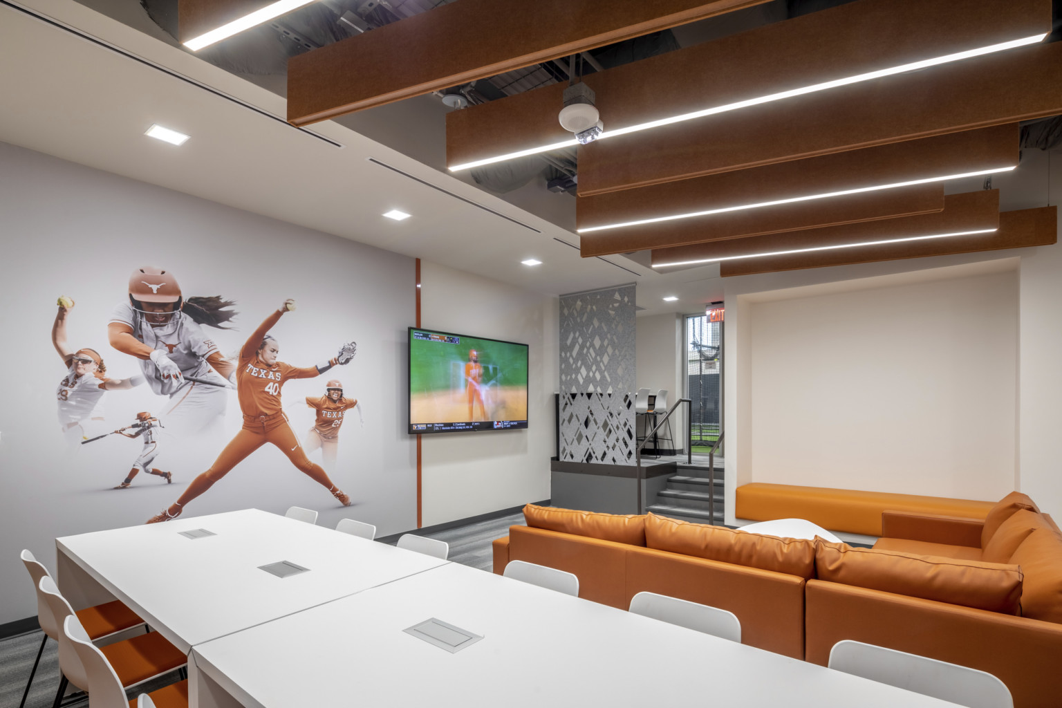 University of Texas Softball Development Facility interior. Softball mural on wall next to screen in front of orange couch