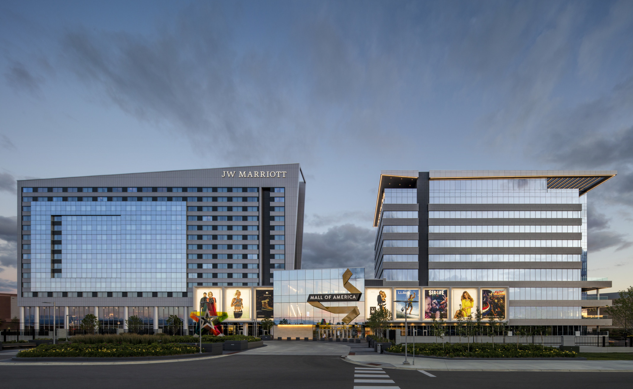 Mall of America entry with illuminated signage connecting 2 grey angled buildings. Left building labelled JW Marriott Mall of America entry with illuminated signage connecting 2 grey angled buildings. Left building labelled JW Marriott